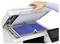 Une main soulève le couvercle d'une photocopieuse, dévoilant un livre ouvert posé sur la surface de numérisation, prêt à être photocopié.