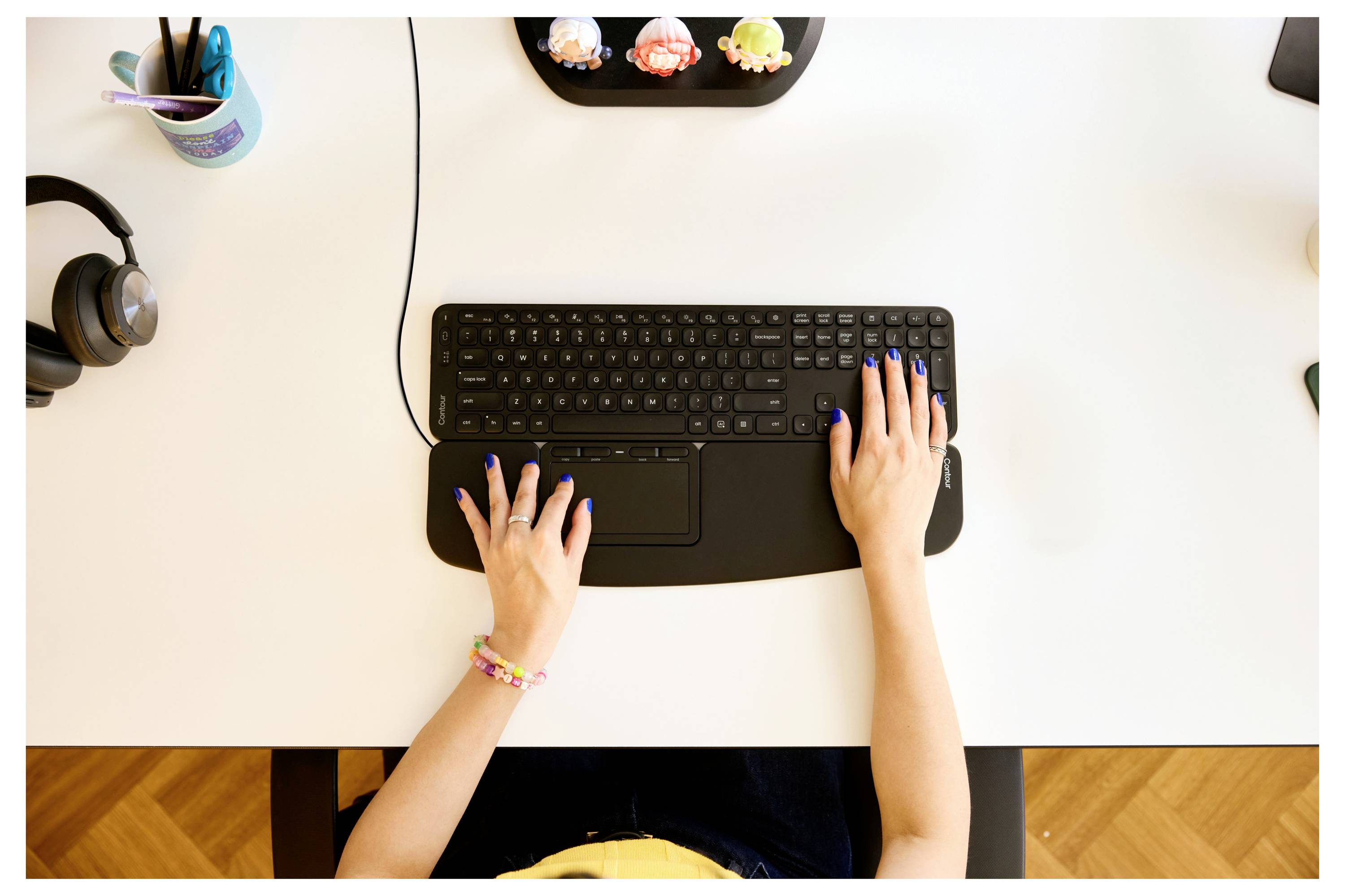 Une personne tape sur un clavier noir à un bureau blanc, avec des objets à proximité en forme de cupcakes colorés.