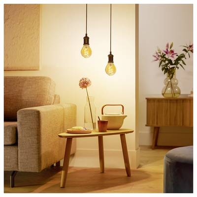 Un salon douillet avec un éclairage chaleureux. Deux luminaires suspendus au-dessus d'une table en bois, un canapé beige et un bahut avec des fleurs roses dans un vase.