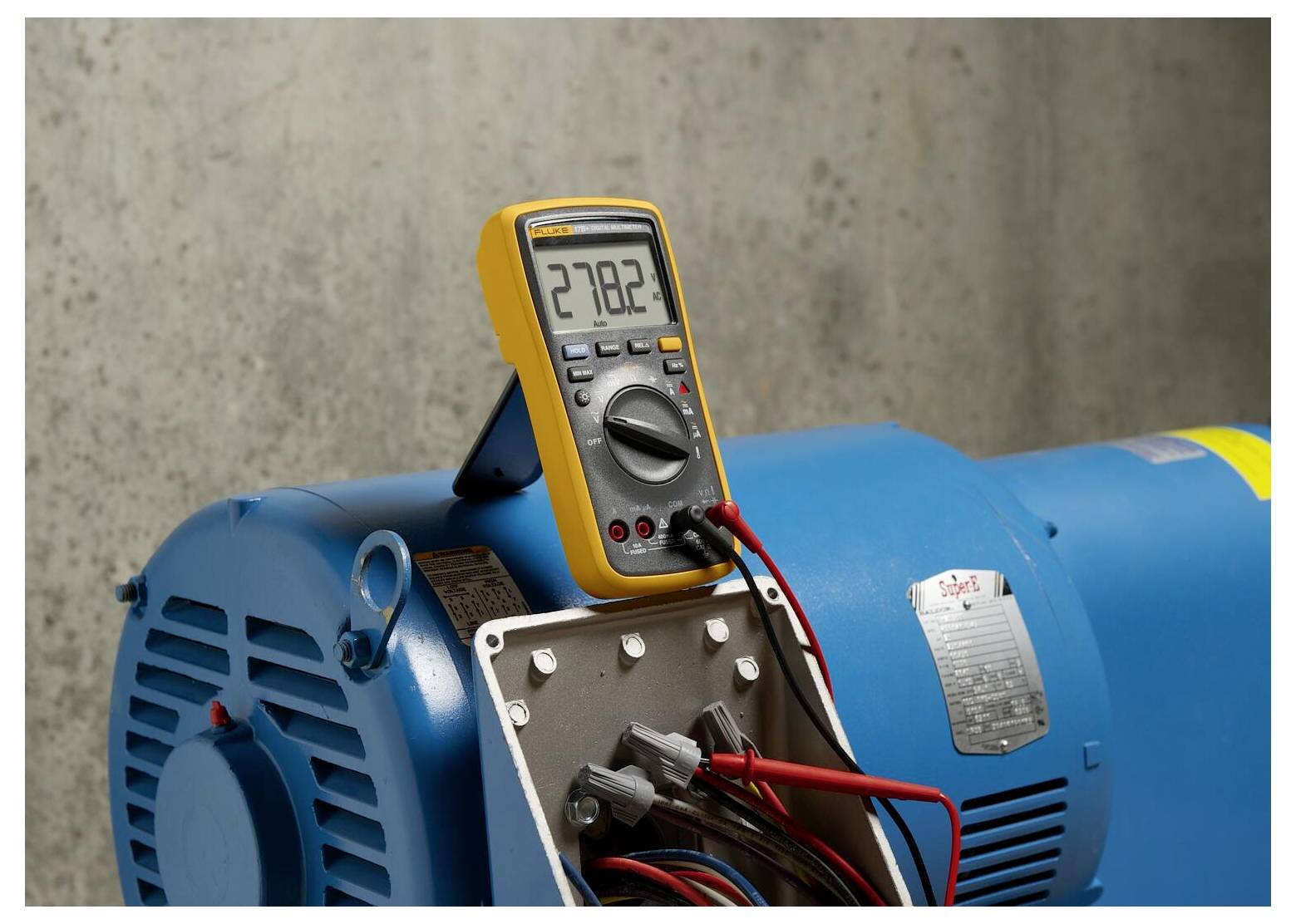 Un multimètre numérique affiche '278,2', connecté à un moteur industriel bleu, mesurant la tension électrique.