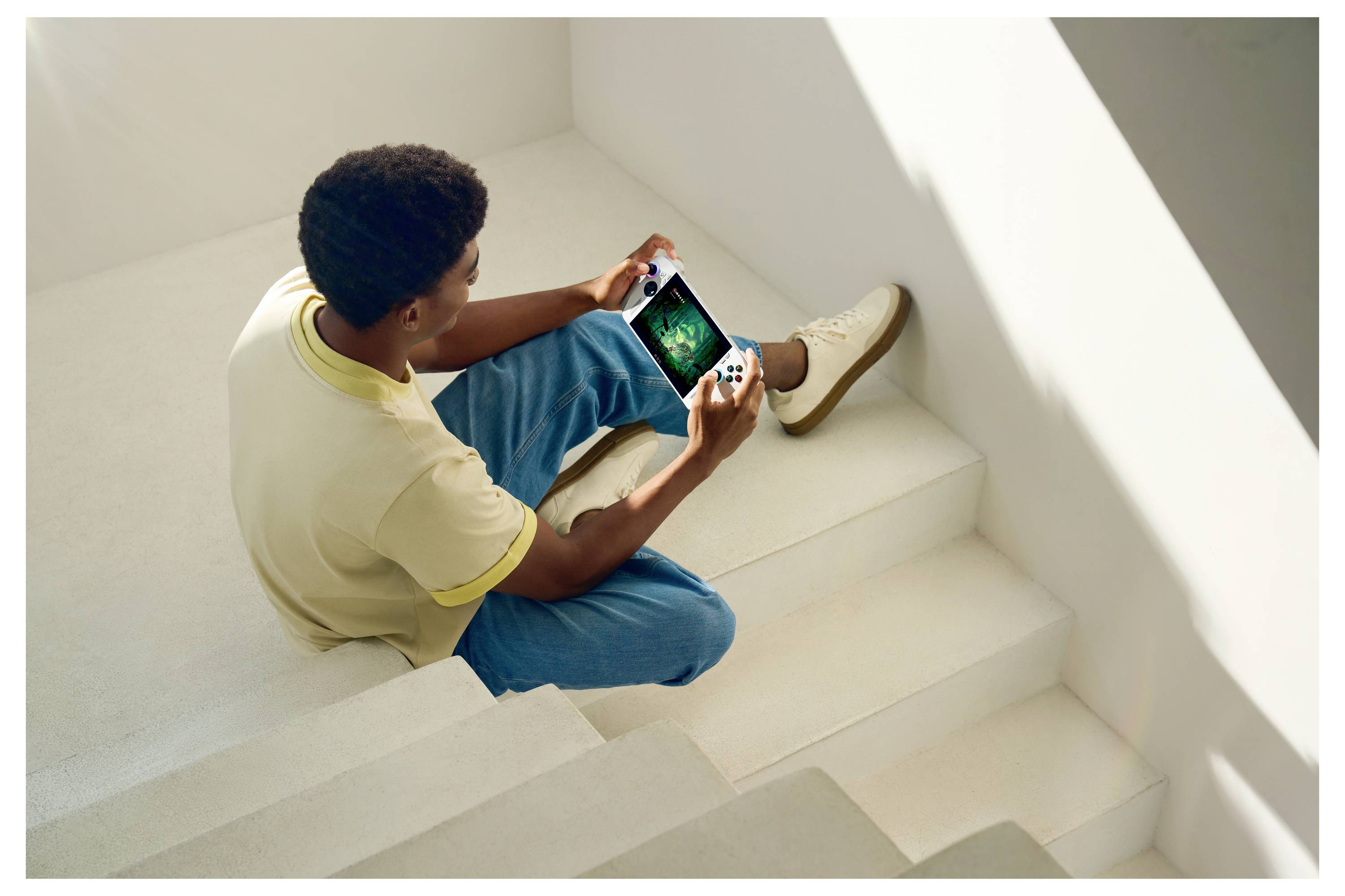 Une personne vêtue de vêtements décontractés est assise sur des escaliers blancs, tenant une console de jeux vidéo et jouant à un jeu. Environnement lumineux, minimaliste, baigné de lumière naturelle.