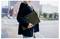 Une personne portant un blazer sombre tient un ordinateur portable Acer, debout sur une rue de ville, avec des immeubles et du trafic flou en arrière-plan.