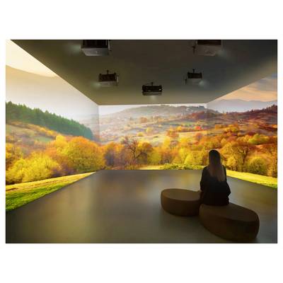 Une personne est assise sur un banc dans une pièce dotée d'écrans immersifs affichant un paysage d'automne, avec des arbres aux couleurs vives et des collines ondulantes.