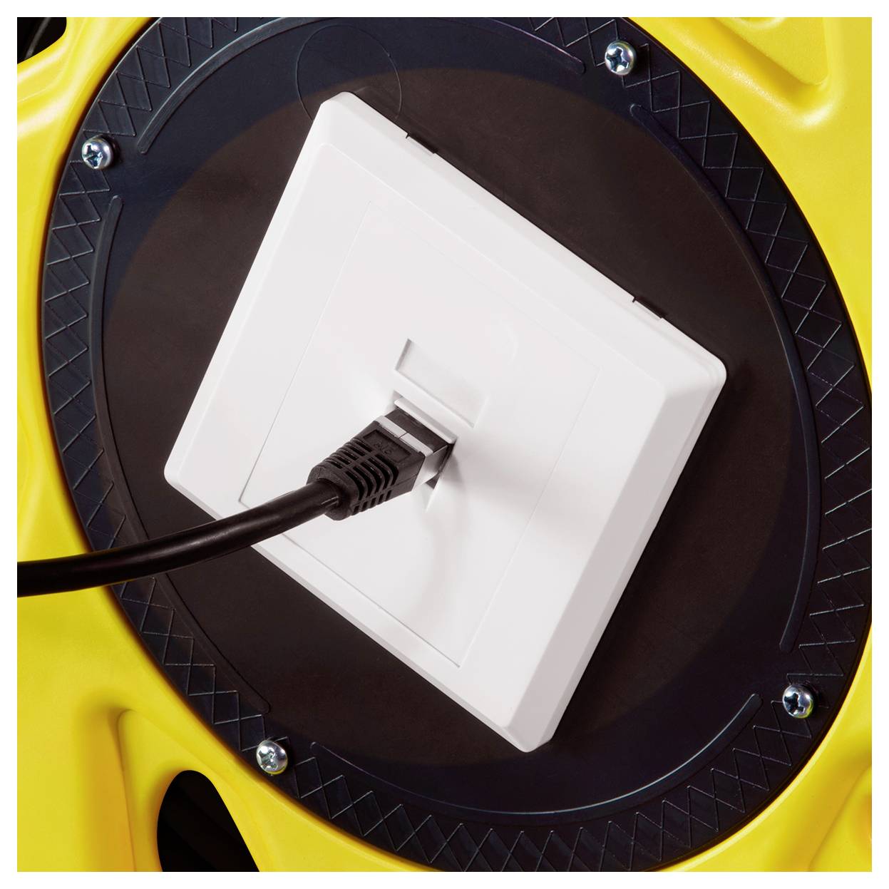 Un câble noir est branché dans une prise murale blanche sur une surface industrielle jaune et noire, suggérant un dispositif de connexion électrique.