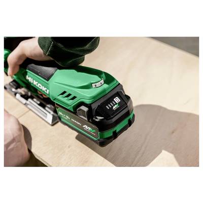 Une personne utilise un outil électrique Hikoki vert sur une surface en bois, concentrée sur un travail de précision. L'outil présente une marque et des commandes bien visibles.