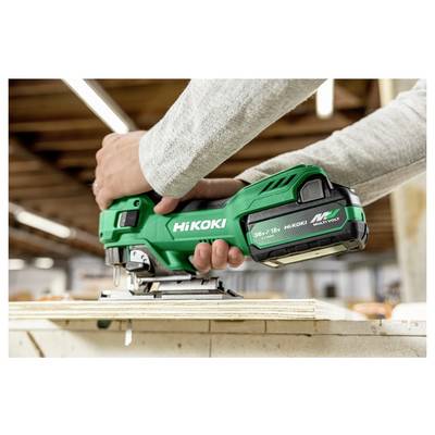 Une personne utilisant une scie sauteuse sans fil verte sur une surface en bois dans un atelier, en mettant l'accent sur la marque de l'outil et sa caractéristique d'alimentation par batterie.