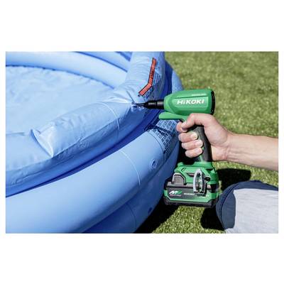 Une personne utilise une pompe sans fil verte pour gonfler une piscine gonflable bleue dans une zone herbeuse. La pompe est étiquetée « HiKOKI ».