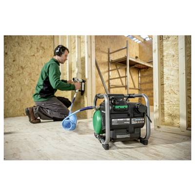 Homme utilisant un cloueur pneumatique connecté à un petit compresseur d'air portable dans une pièce en bois partiellement construite, portant une protection auditive.
