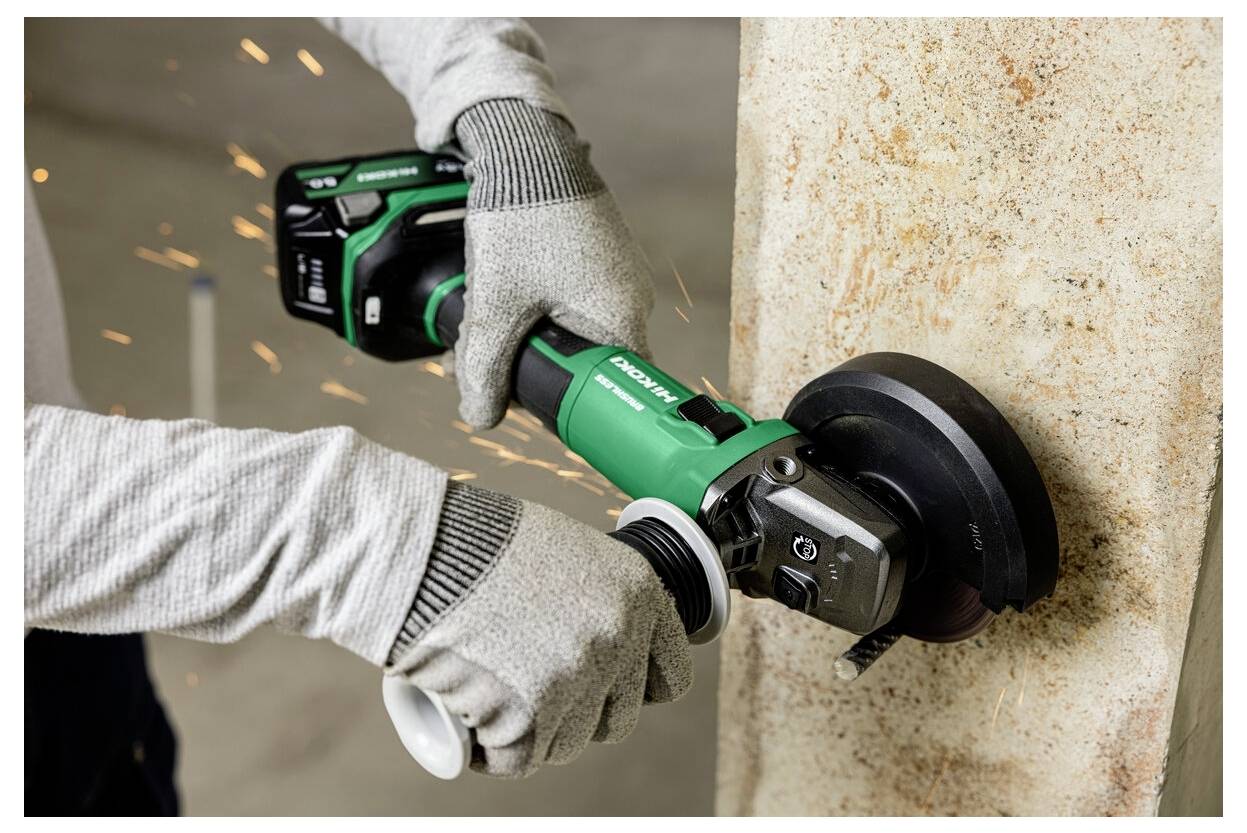 Une personne portant des gants de protection utilise une meuleuse d'angle électrique pour découper un mur en béton, créant des étincelles pendant que l'outil est en marche.