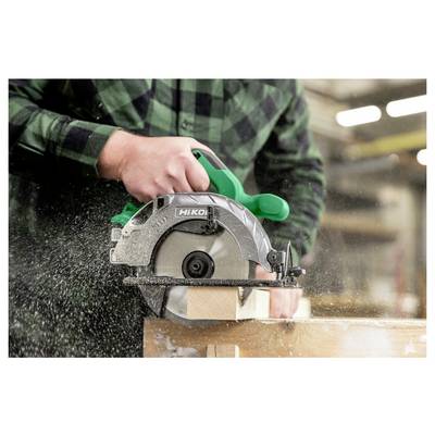Une personne utilise une scie circulaire pour couper du bois, créant de la sciure. La scie à poignée verte est en mouvement, avec de la sciure qui se disperse vers l'extérieur.