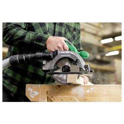 Une personne portant une chemise à carreaux verts utilise une scie circulaire pour couper un morceau de bois sur un établi, avec des copeaux de bois en mouvement.