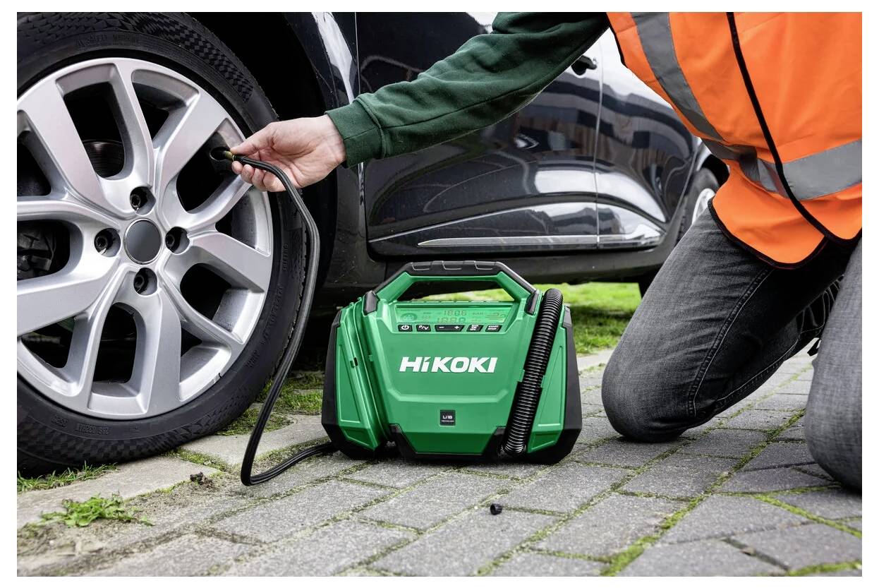 « Une personne gonflant un pneu de voiture à l'aide d'un compresseur d'air HiKOKI vert sur une surface pavée, portant un gilet de sécurité orange. »