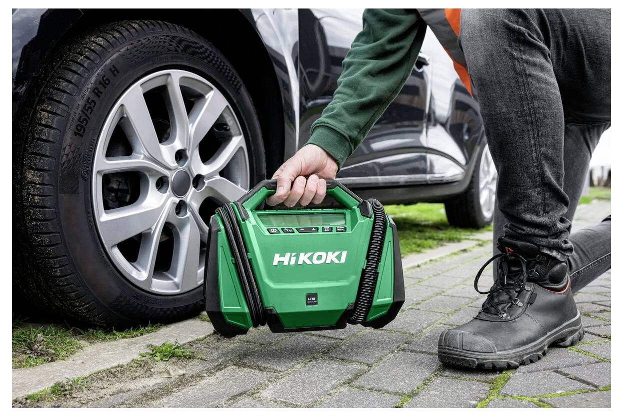 Une personne s'accroupit à côté d'un pneu de voiture, tenant un compresseur d'air portable HiKOKI vert, indiquant le gonflage ou l'entretien du pneu.