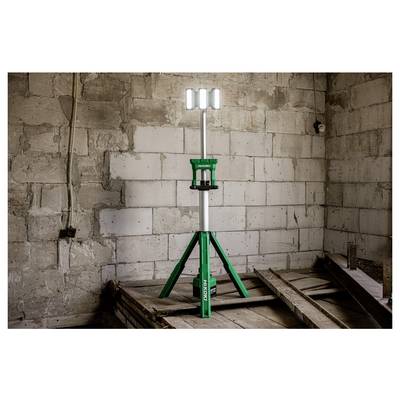 Un projecteur de chantier vert monté sur trépied se tient dans une pièce en cours de construction aux murs de briques nues, fournissant un éclairage portable sur le site.