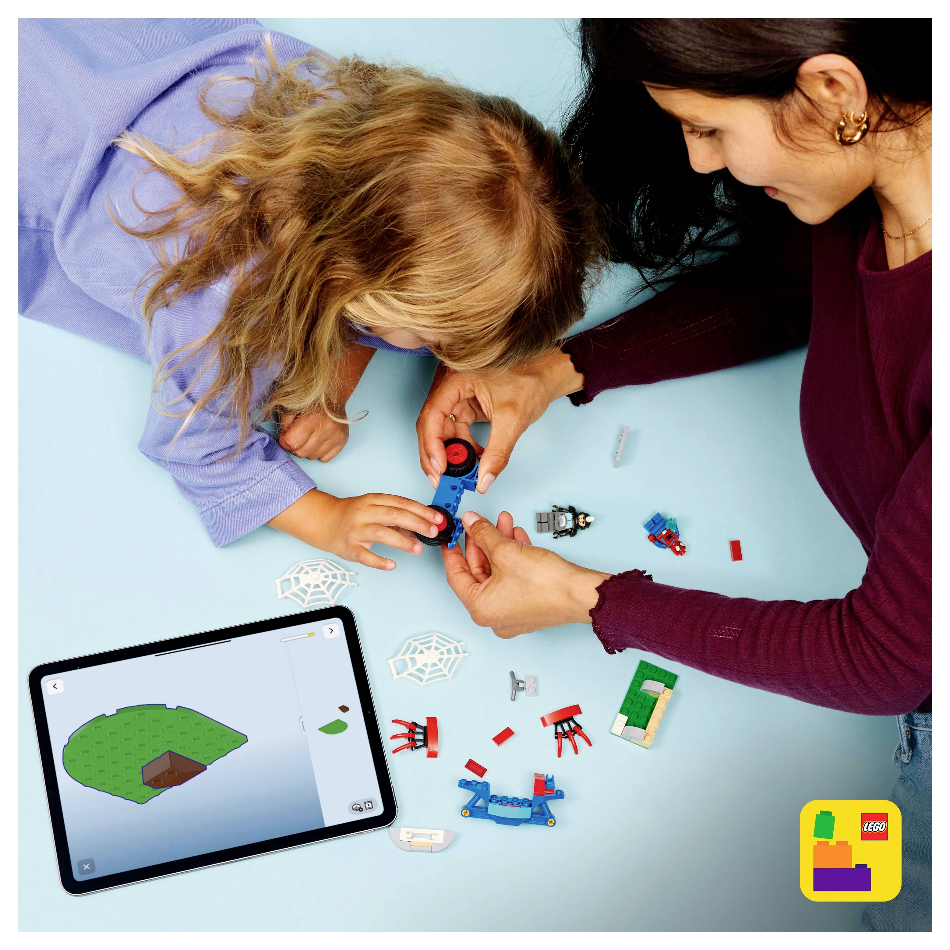 Un enfant et un adulte construisent un modèle coloré avec de petits blocs sur une surface bleue, en suivant les instructions affichées sur une tablette.