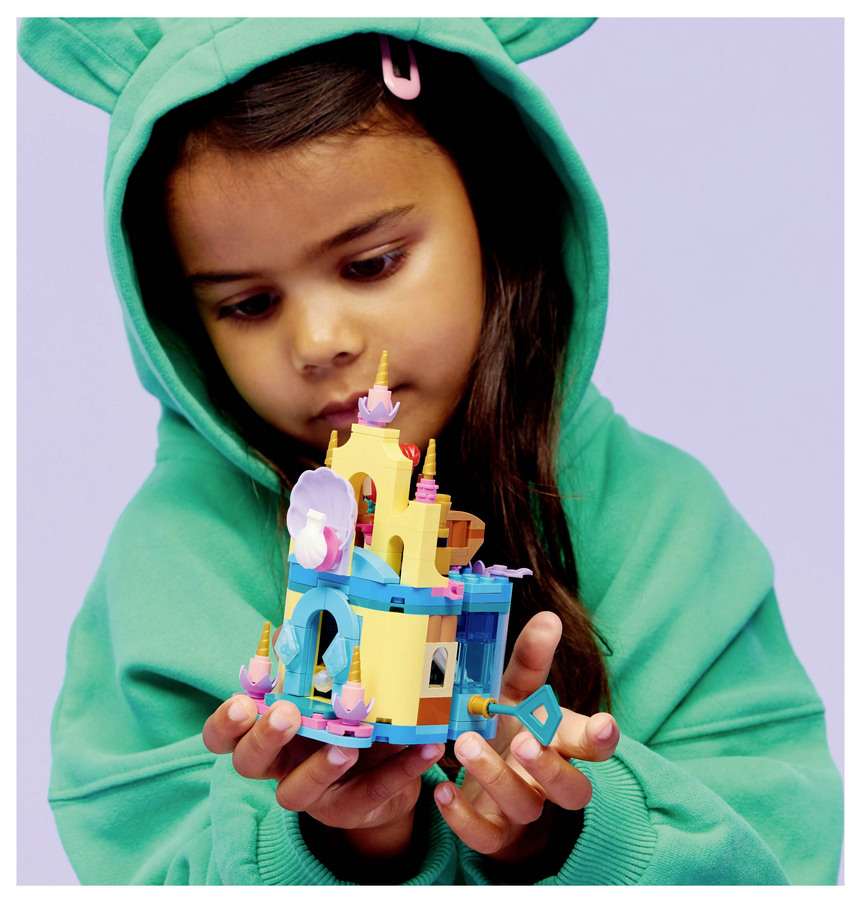 Un enfant portant un sweat à capuche vert examine soigneusement un modèle de château LEGO coloré, concentré sur ses moindres détails.