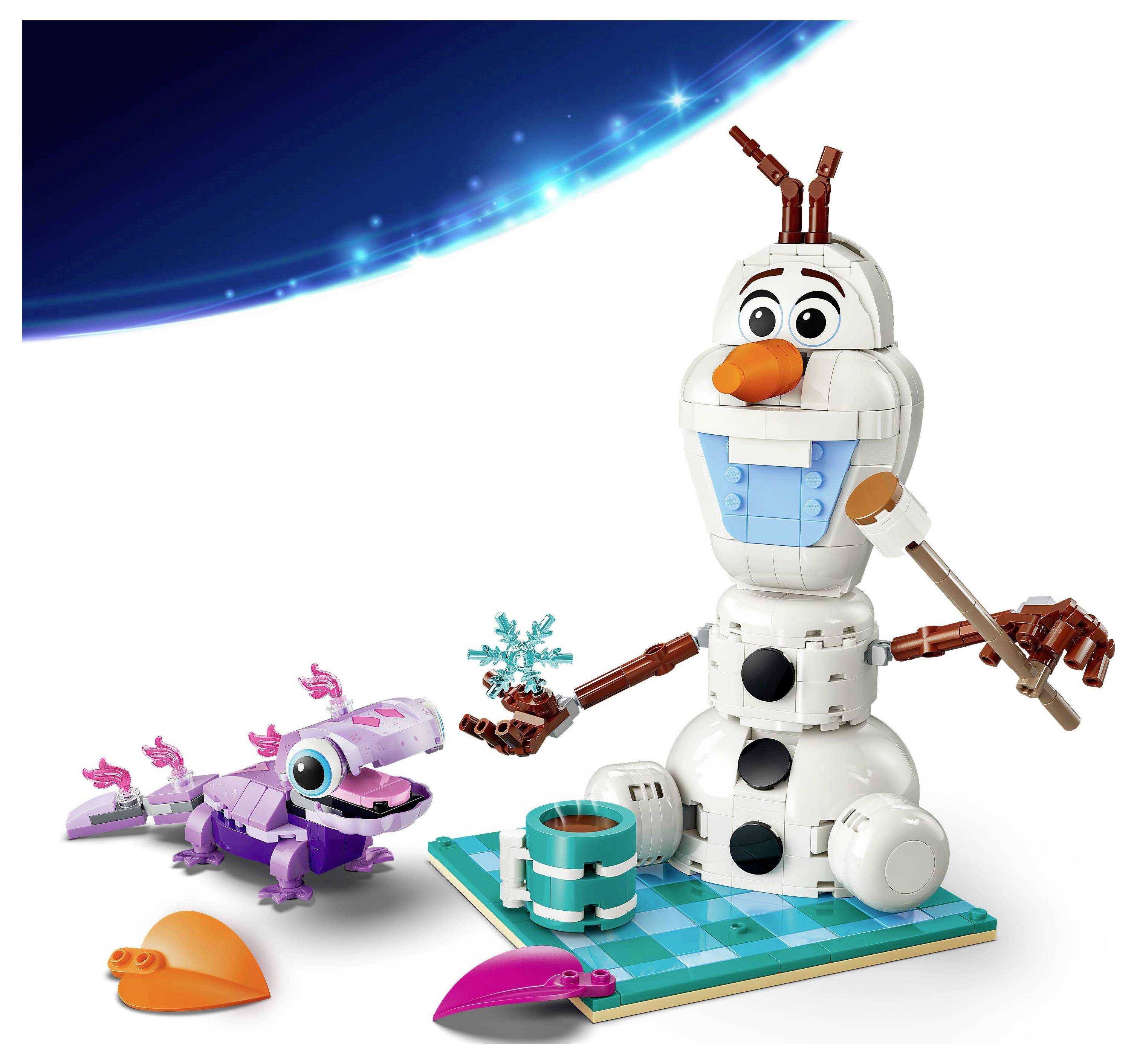 Un bonhomme de neige LEGO tenant un pinceau et une pièce en forme de cœur bleue, assis sur une base verte, avec un lézard violet à proximité.