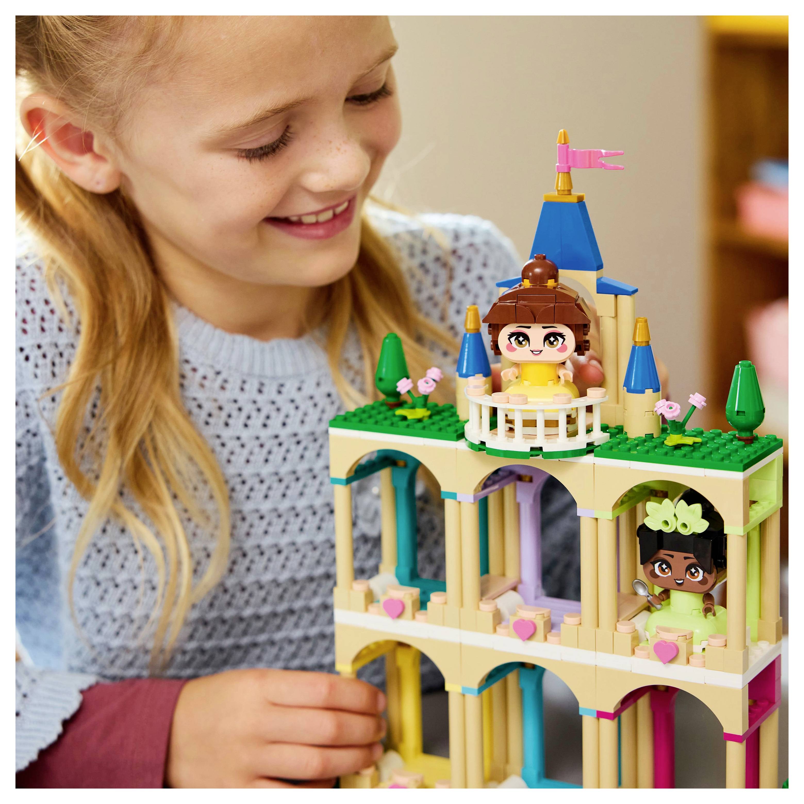 Un enfant sourit tout en jouant avec un château de jouet coloré, avec de petites figurines et des tourelles, sur une table en bois.