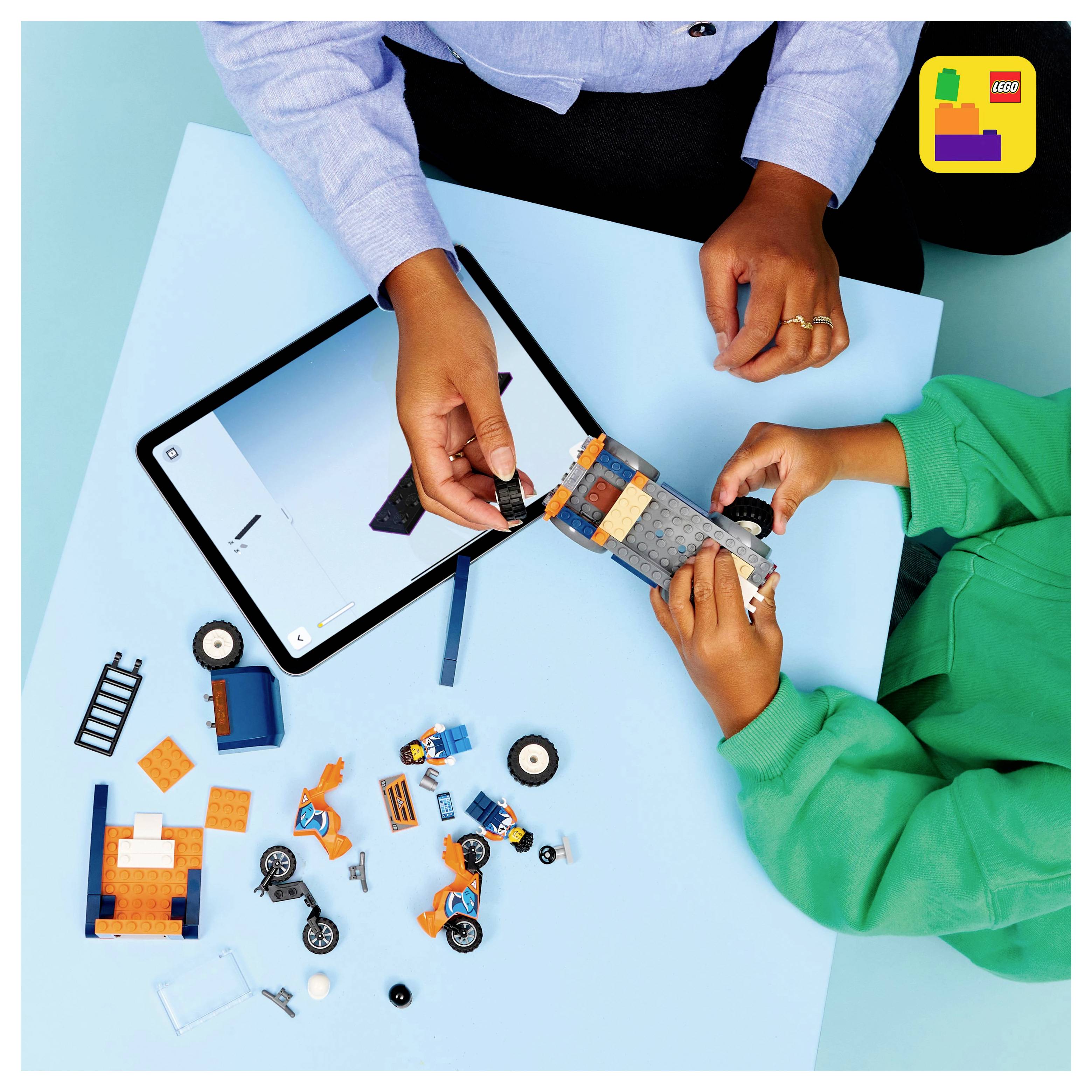 Deux personnes construisent un véhicule LEGO avec différentes pièces, à côté d'une tablette affichant des instructions. Logo LEGO dans le coin.
