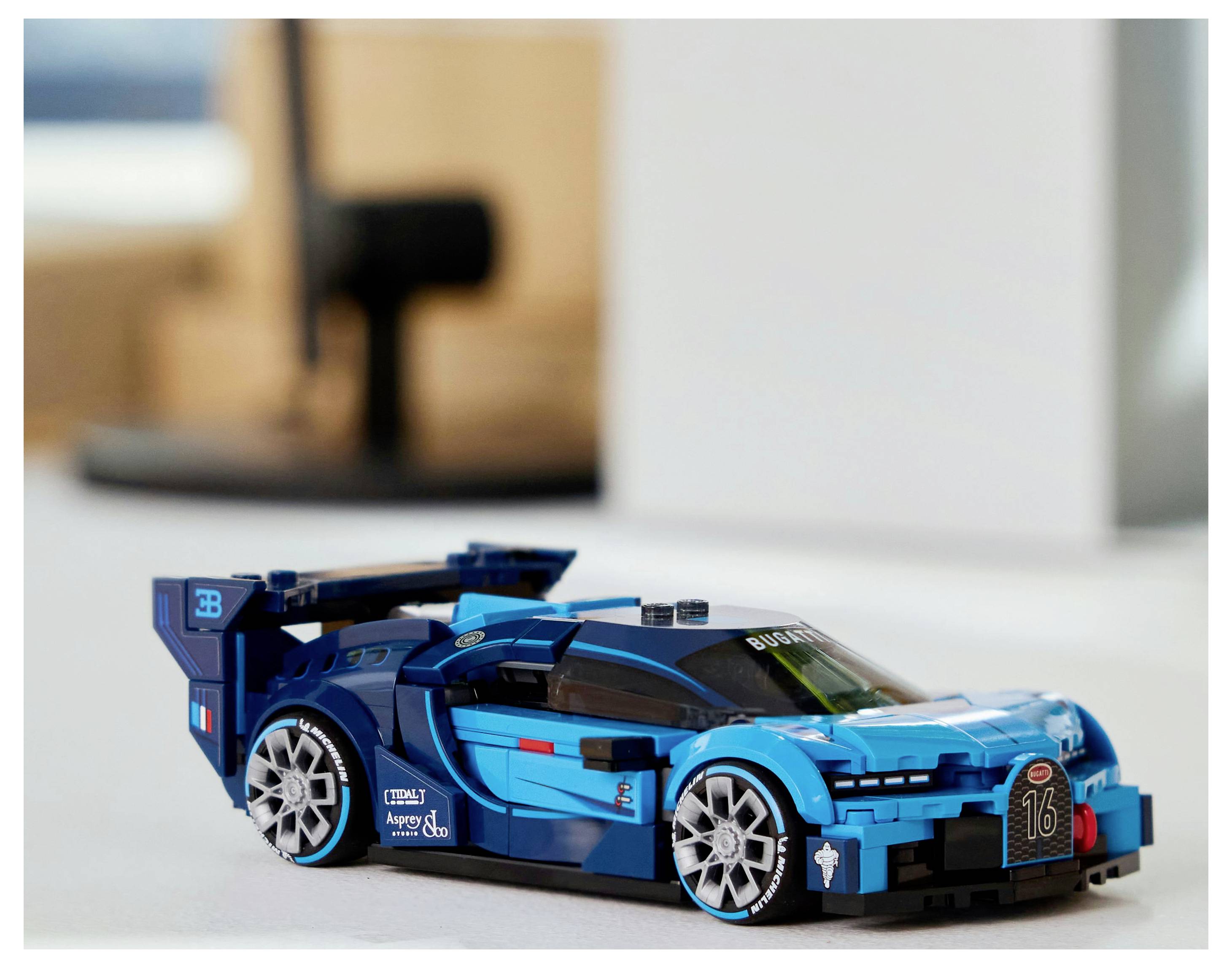 Une voiture de course miniature bleue posée sur une table, arborant un design sportif avec des caractéristiques aérodynamiques et des structures de roues détaillées.