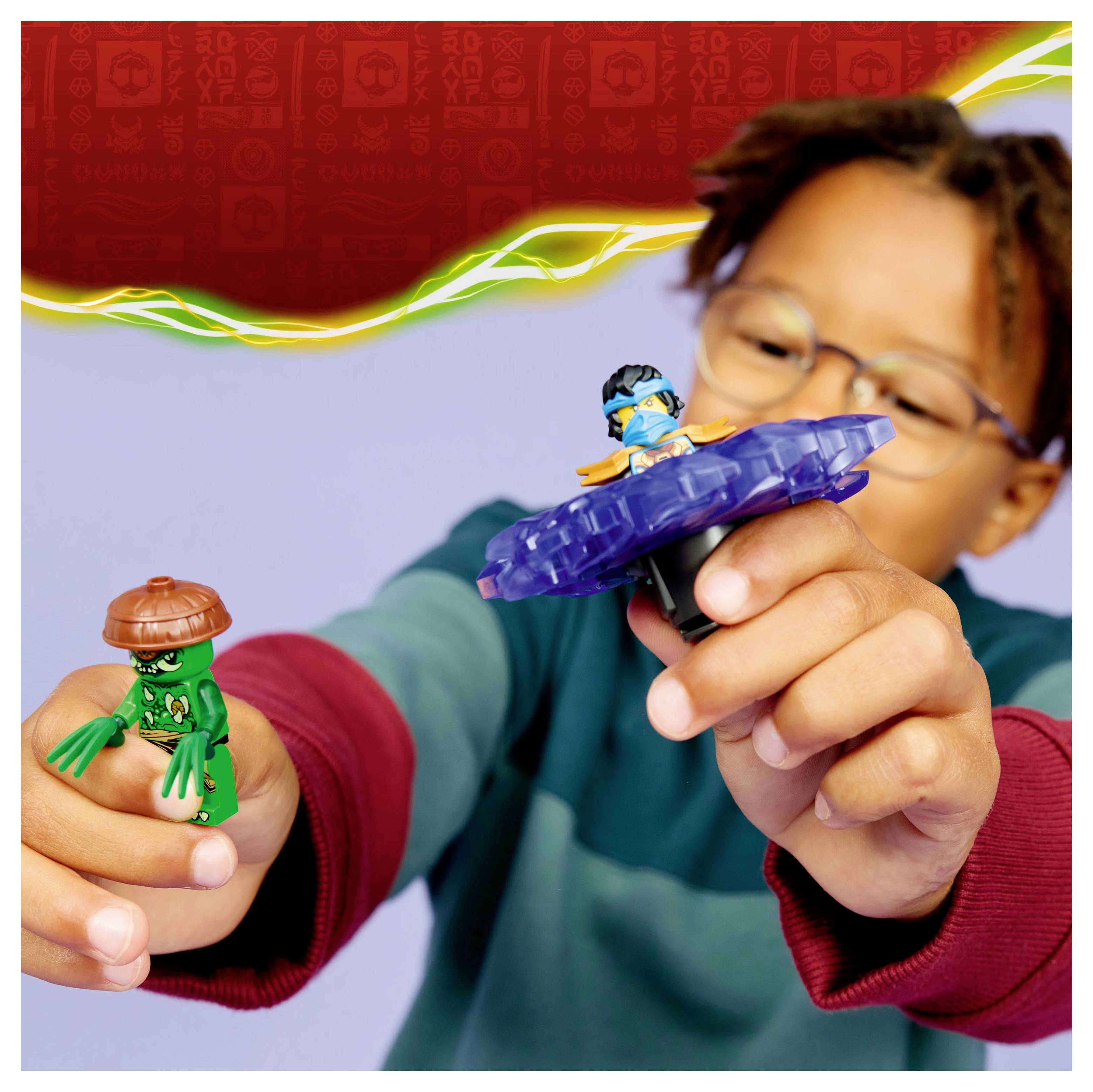 Un enfant tient deux figurines : un personnage vert portant un casque brun et un personnage bleu sur une base tournante, contre un fond lumineux.