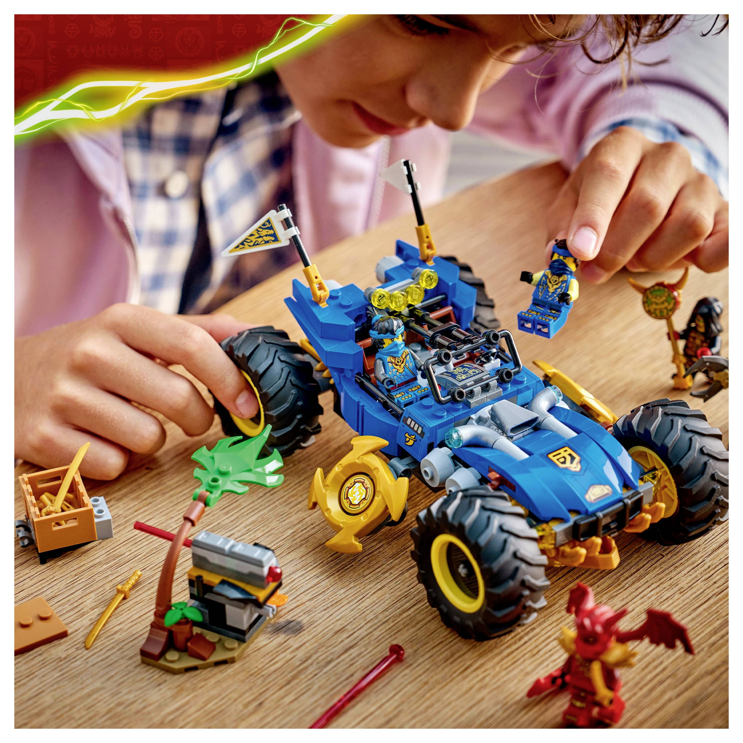 Un enfant joue avec un ensemble de véhicules détaillé comprenant une voiture bleue aux grandes roues, entourée de petites figurines fantastiques et d'accessoires.