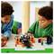 Deux enfants sont occupés à construire et à jouer avec un ensemble de blocs sur une table, comprenant un portail miniature et des personnages.
