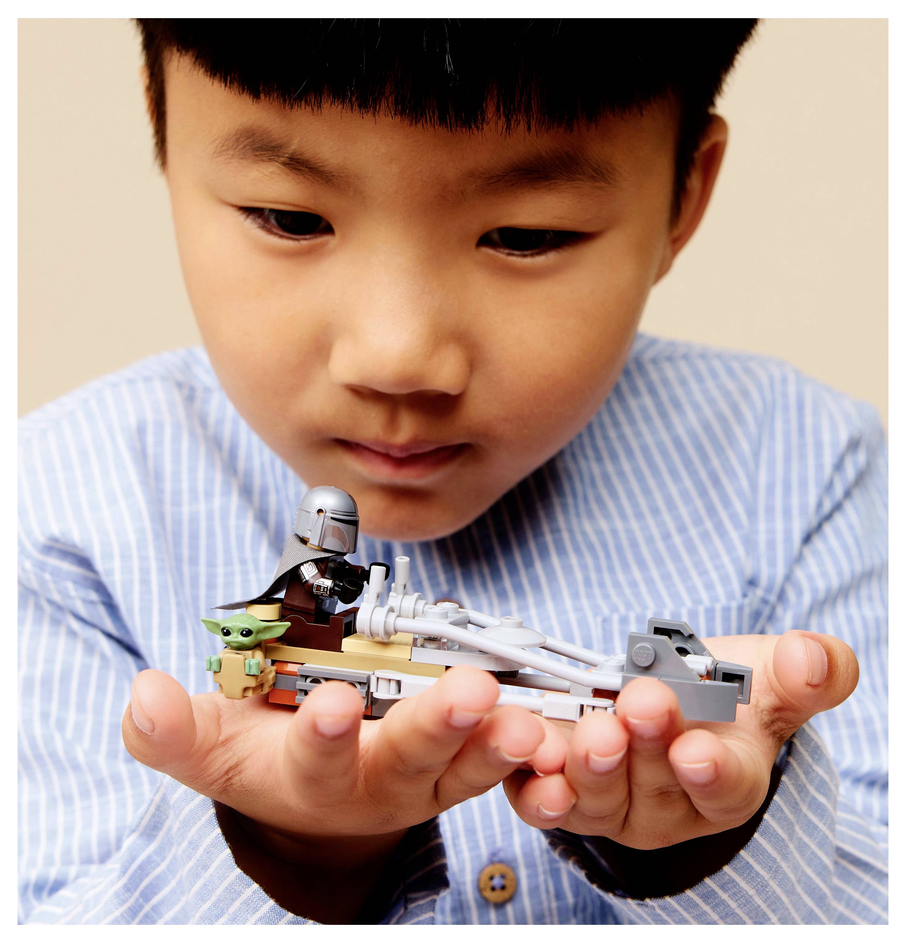 Un enfant tient un ensemble LEGO représentant une petite figurine en armure et une figurine verte, toutes deux ressemblant à des personnages d'une série de science-fiction populaire.