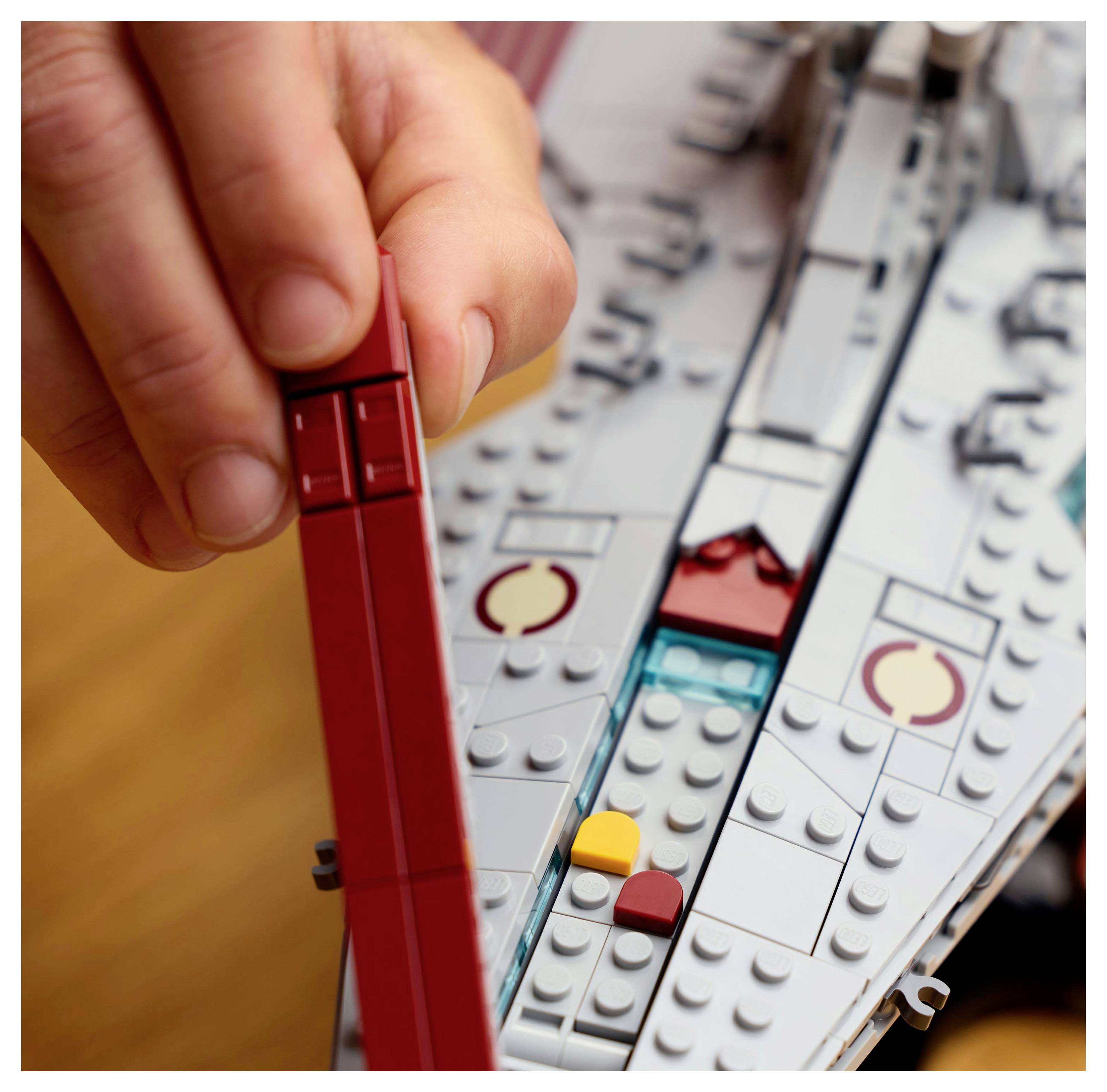 «Une main tient une brique rouge au-dessus d'un modèle de vaisseau spatial partiellement assemblé construit avec des briques en plastique emboîtables.»