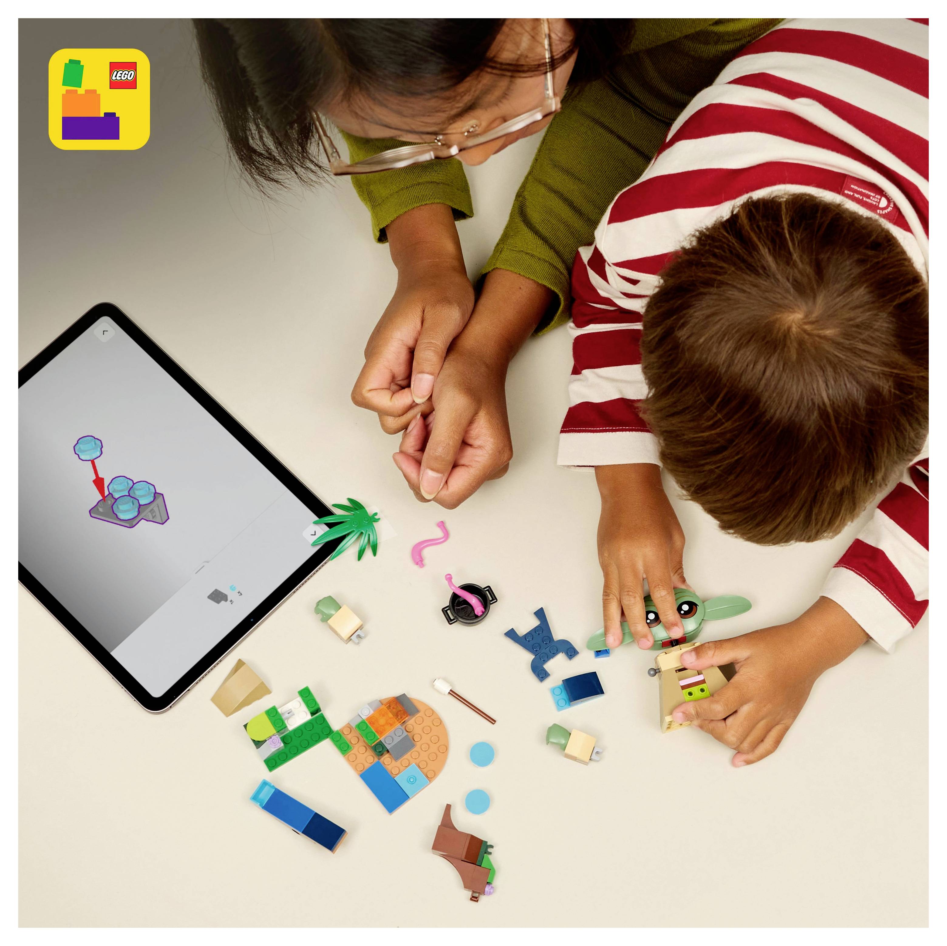 Un enfant et un adulte jouent avec des briques LEGO sur une table à côté d'une tablette affichant un modèle LEGO. Le logo LEGO est dans le coin supérieur gauche.