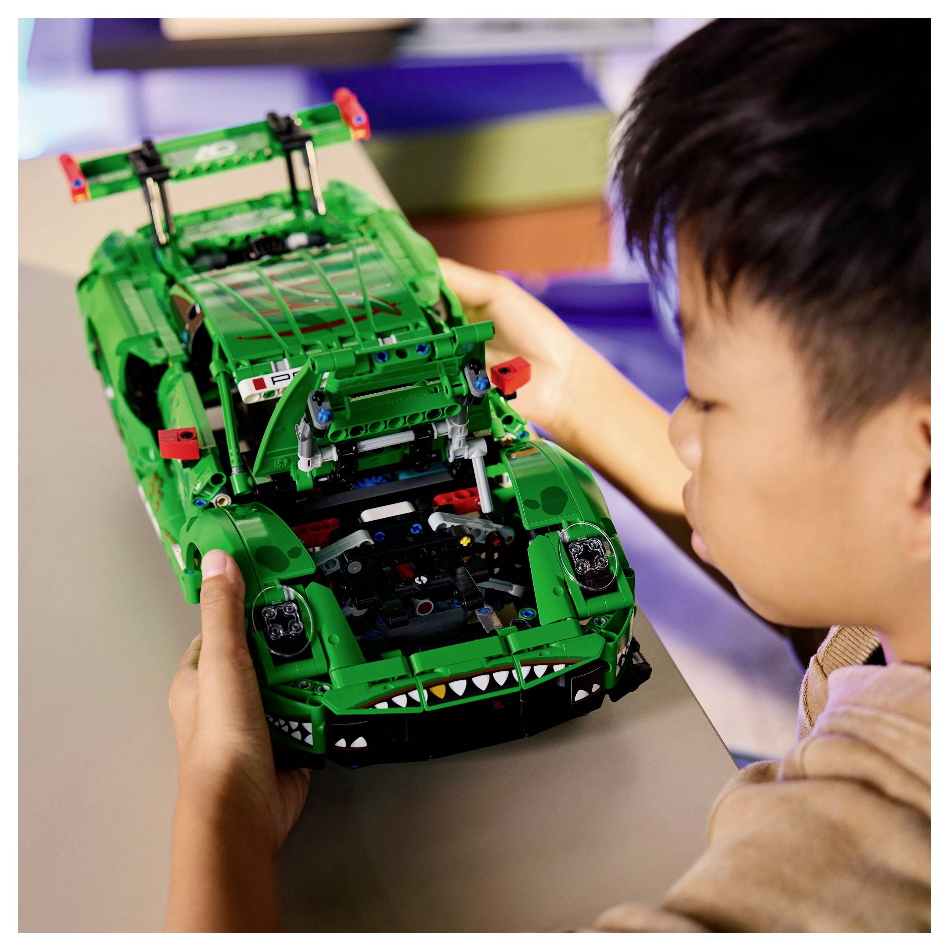 Un enfant assemble une voiture jouet verte avec des détails complexes sur une table, concentré sur le placement précis des pièces.