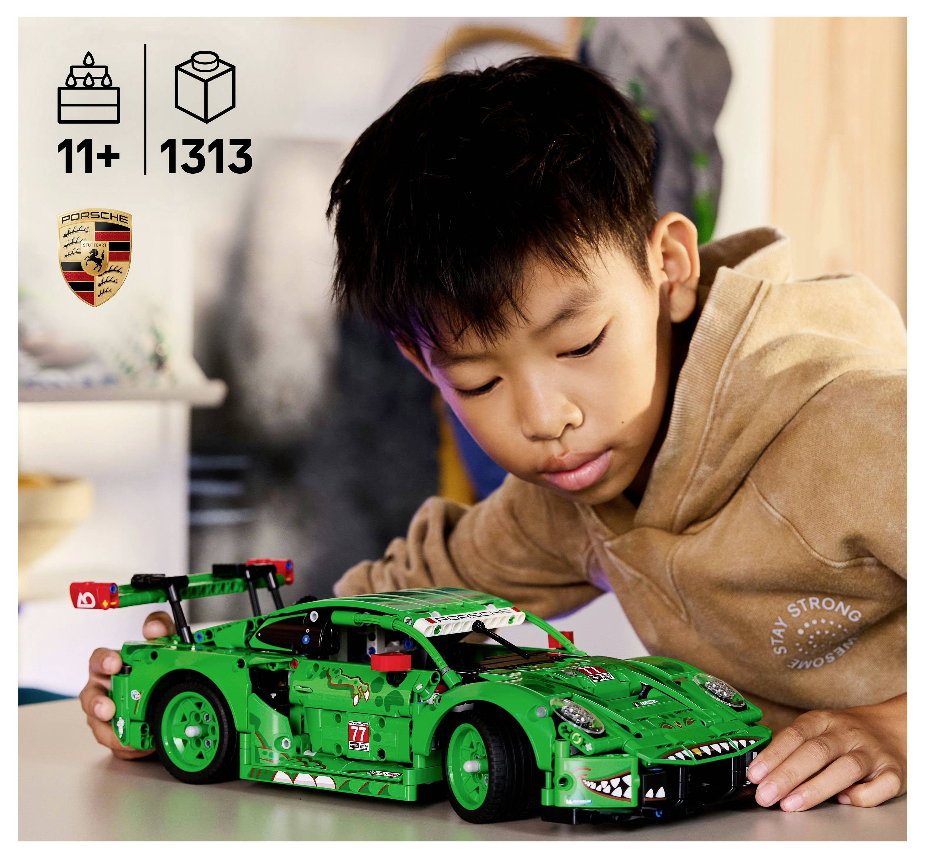 Un enfant portant un sweat à capuche admire une voiture de course verte sur une table. L'image présente les logos Lego et Porsche, un âge recommandé de 11 ans et plus, et un nombre de 1313 pièces.