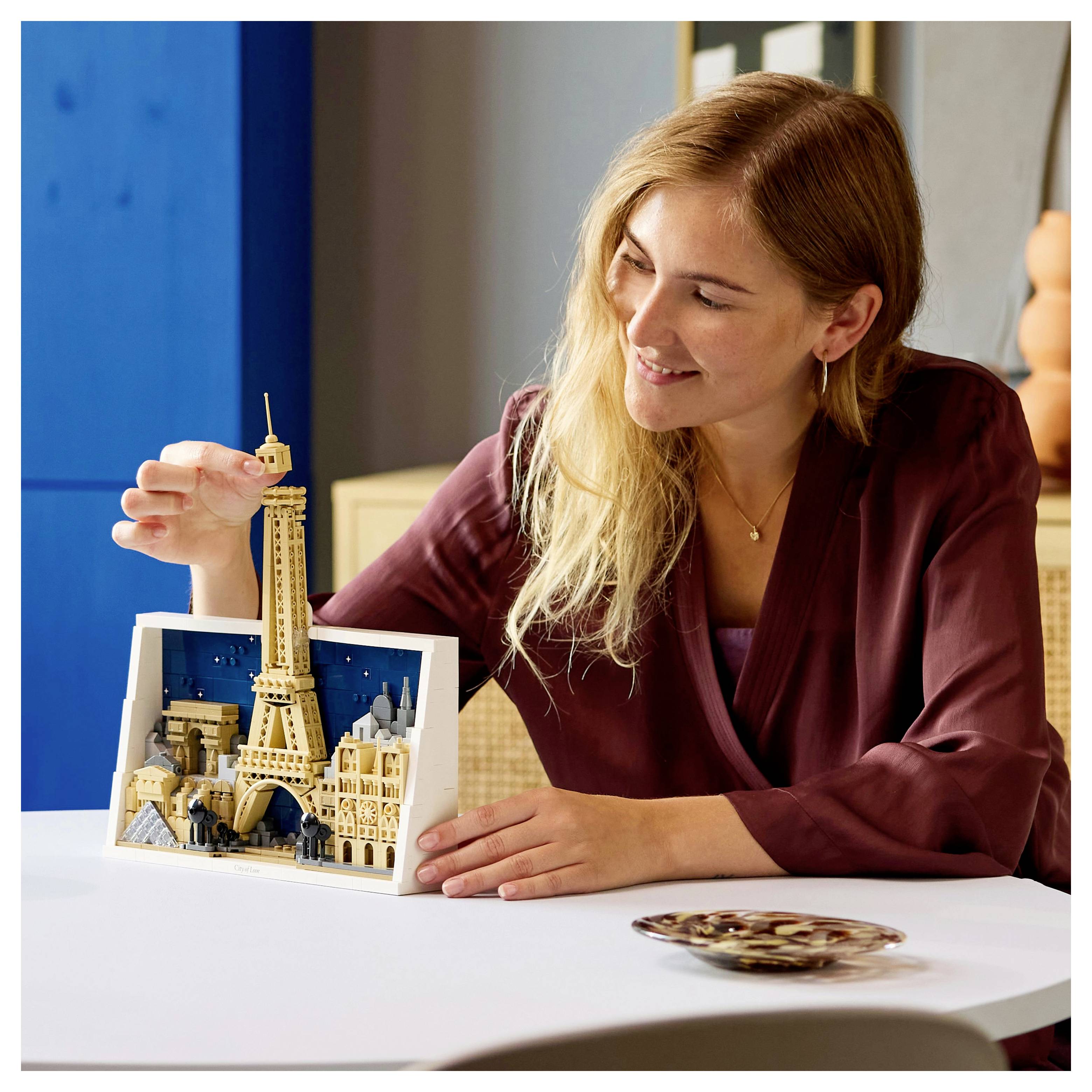 Une personne sourit en assemblant un modèle miniature détaillé de la Tour Eiffel sur une table, indiquant une activité créative et captivante.