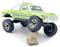 Un petit camion de ramassage jouet vert avec de grandes roues tout-terrain est en équilibre sur une petite pile de rochers, mettant en valeur son design robuste.