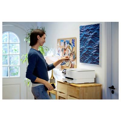 Une personne place une photo depuis un smartphone sur une imprimante domestique, se tenant dans une pièce bien éclairée avec un tableau d'affichage et une peinture à proximité.