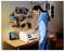 Une personne portant un sweat à capuche bleu clair, debout à un bureau, en train d'imprimer un document. Le bureau est décoré de photos et de petites œuvres d'art.