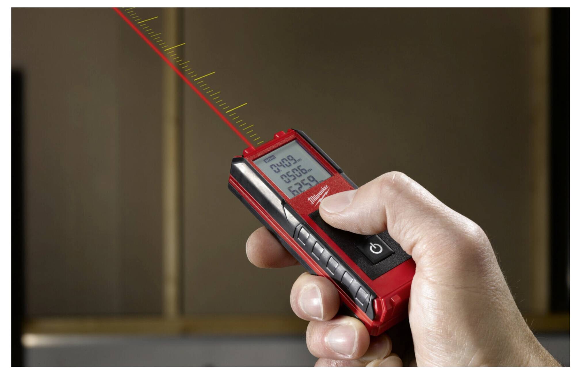 Une main tient un télémètre laser numérique, affichant '25,36 m' sur l'écran, pointé pour mesurer une surface verticale.