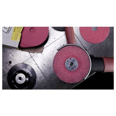 Un outil de ponçage industriel rouge avec un disque abrasif circulaire sur une surface de travail métallique, entouré de disques de ponçage supplémentaires.