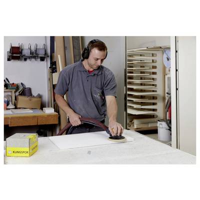 Une personne dans un atelier utilise un ponçoir à main sur un tableau blanc, avec divers outils et matériaux visibles en arrière-plan.