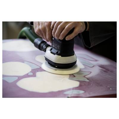 Une personne utilise un ponçoir électrique portable sur une surface présentant des zones irrégulières de différentes couleurs, probablement en préparation pour une peinture ou une rénovation.