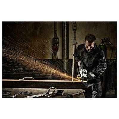 Une personne en tenue de protection utilise un outil de meulage sur une poutre métallique, produisant des étincelles vives dans un atelier industriel faiblement éclairé.