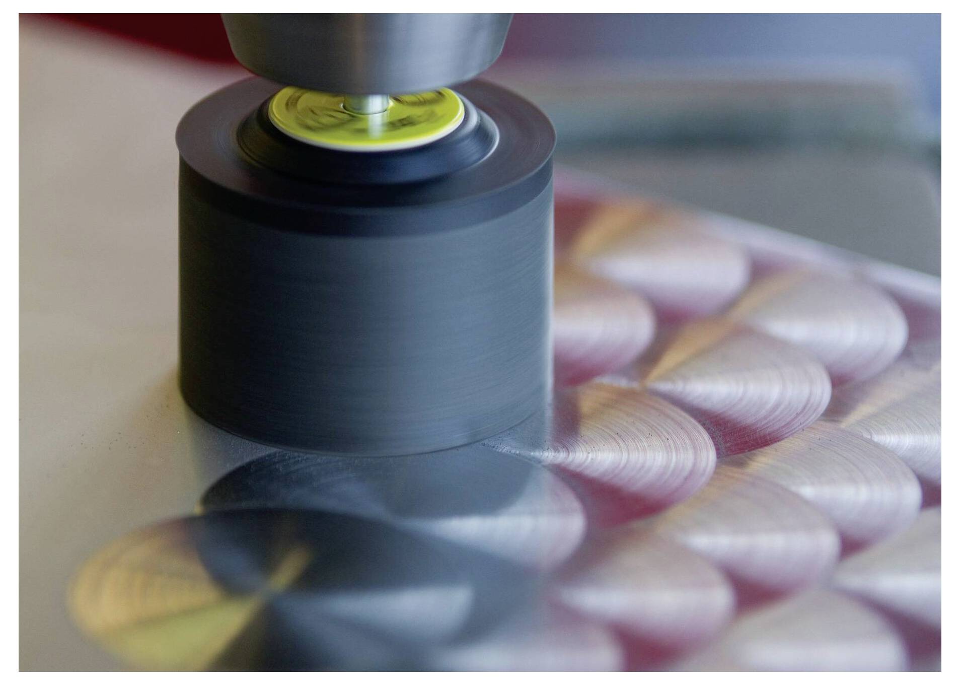 Un disque métallique tournant rapidement sur une surface, créant un motif de sillons circulaires. L'arrière-plan présente des couleurs floues, suggérant un mouvement.