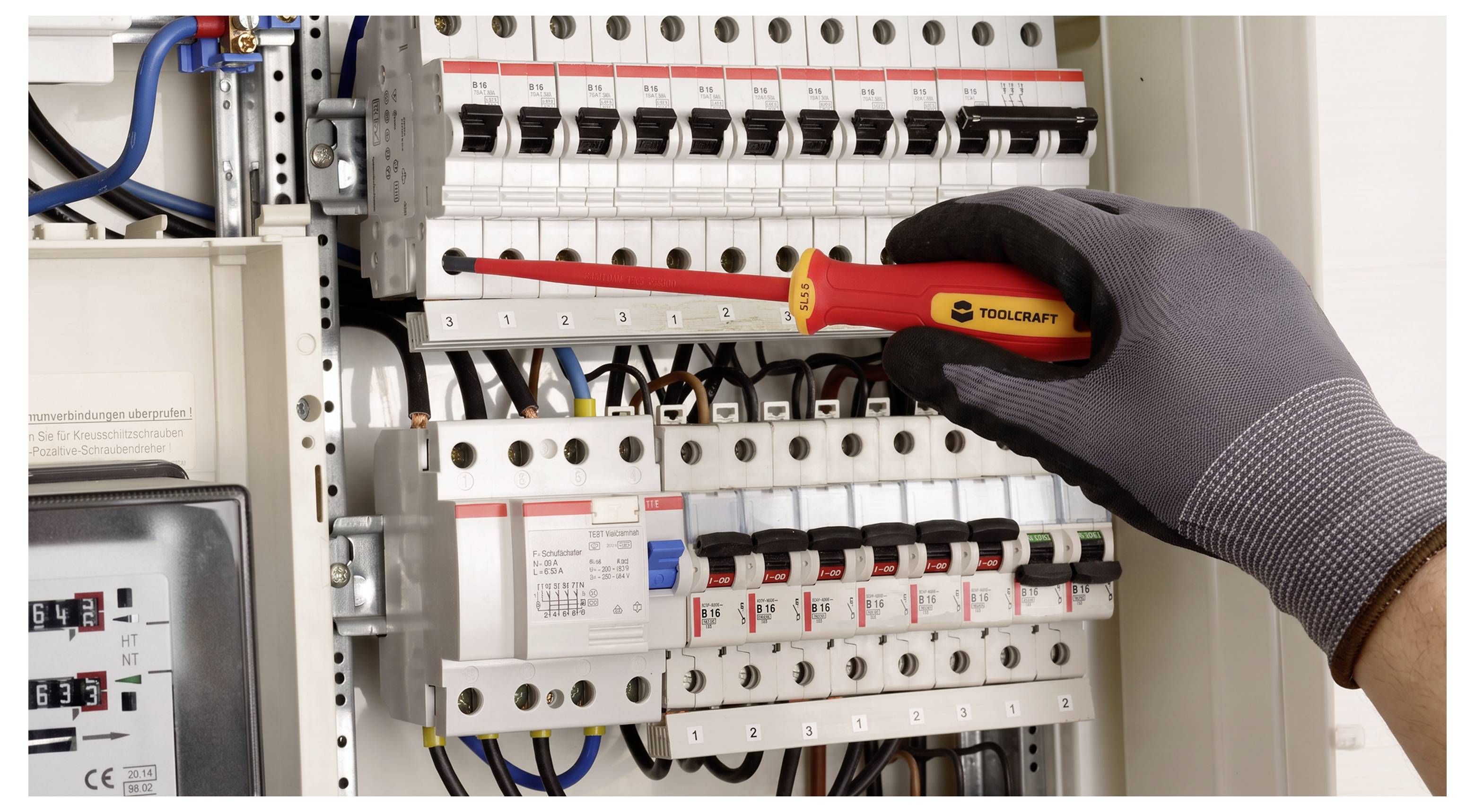 Main gantée qui utilise un tournevis pour serrer un disjoncteur dans un panneau électrique avec des rangées de disjoncteurs et de câblage.