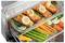 Filets de saumon garnis de citron et d'herbes sur un plateau dans un four, avec des carottes, des asperges, des poivrons et du chou-fleur sur la grille en-dessous.