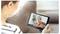 Une personne tient une tablette, en train de faire un appel vidéo avec une autre personne. L'écran affiche un adulte âgé aux cheveux gris, souriant chaleureusement.