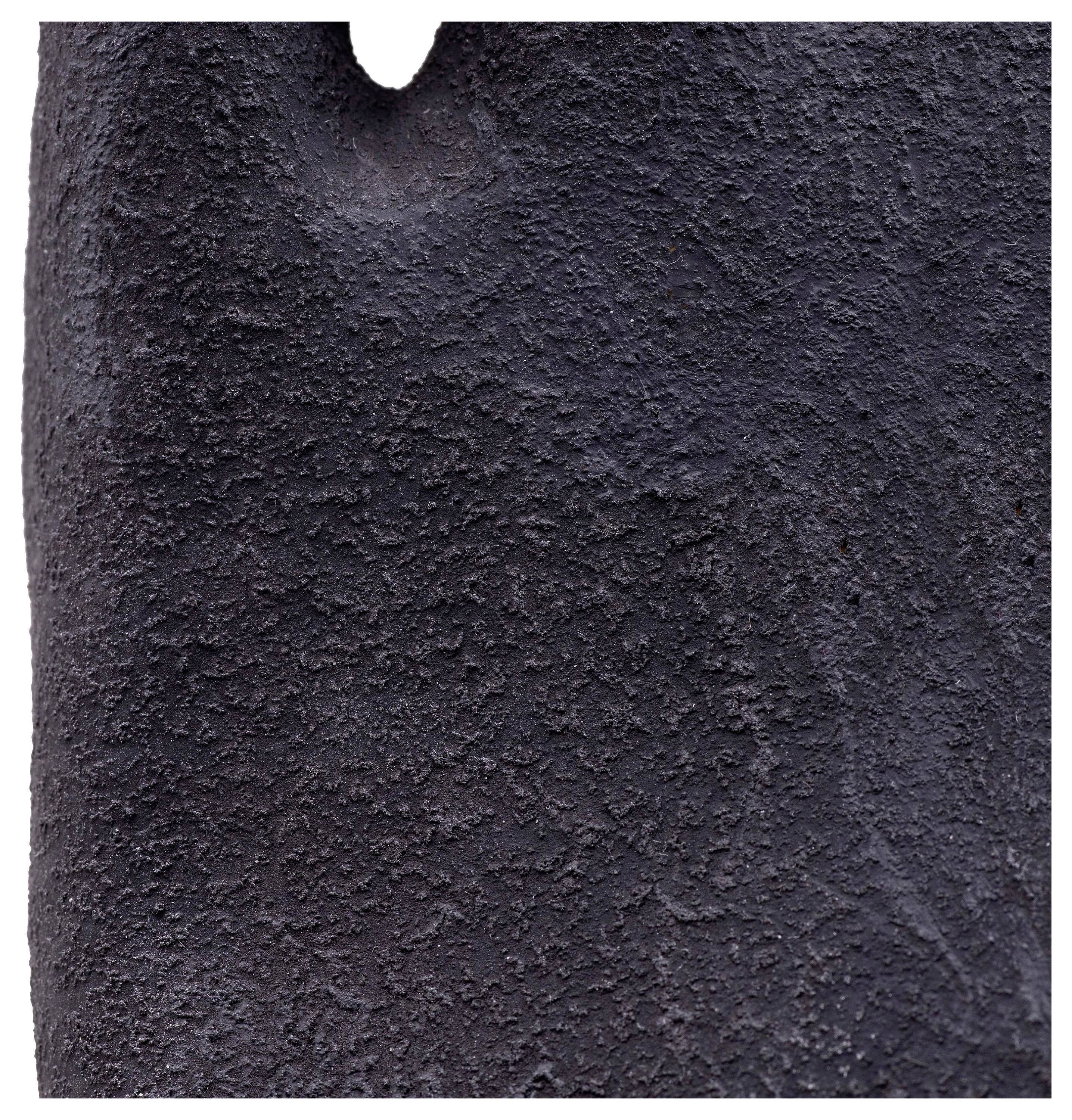 Une image en gros plan d'une surface sombre et texturée, ressemblant possiblement à de la roche volcanique ou de l'asphalte, présentant une légère indentation au sommet.