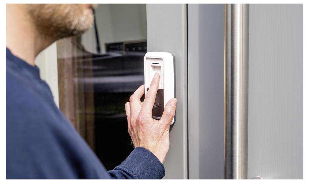 Une personne utilise un lecteur d'empreinte digitale sur une porte, probablement pour déverrouiller ou accéder à une zone sécurisée. L'accent est mis sur la main et l'appareil.