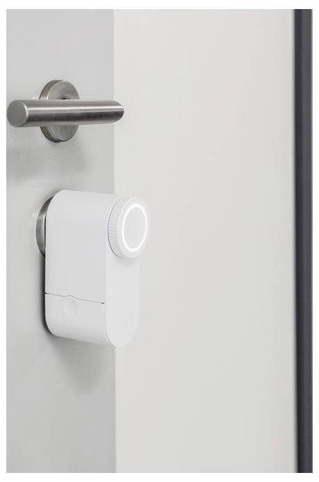 Un verrou intelligent blanc est installé sur une porte, présentant un bouton rond et un design minimaliste, à côté d'une poignée horizontale.