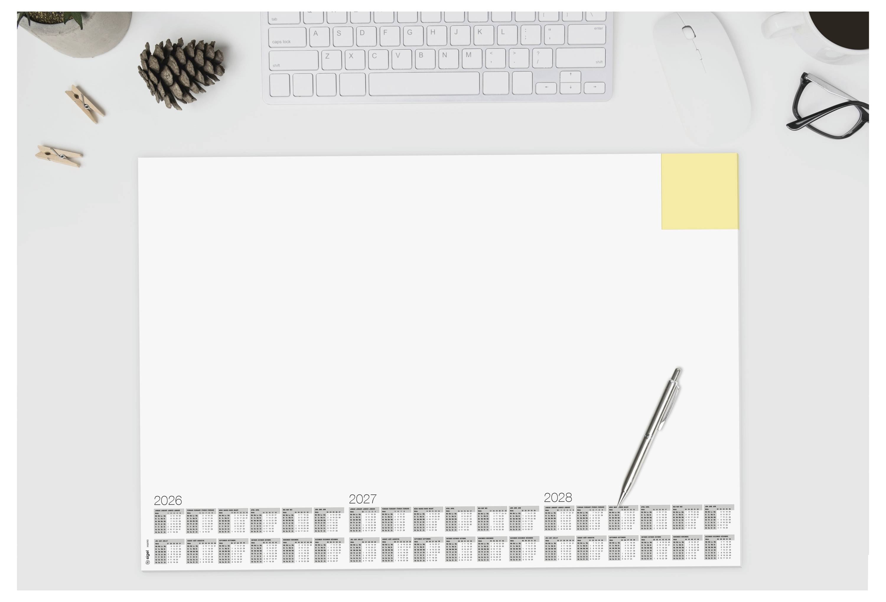 Un aménagement de bureau minimaliste avec un clavier, une tasse, une souris et un agenda présentant des calendriers annuels pour 2026-2028 et un stylo posé sur le dessus.