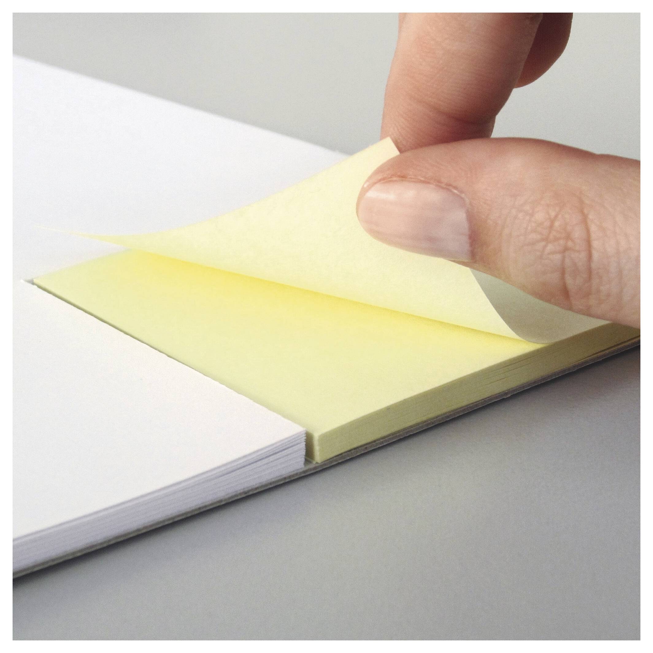 Une main qui décolle un post-it jaune d'un bloc-notes, soulignant l'action de prendre des notes ou de laisser un message.